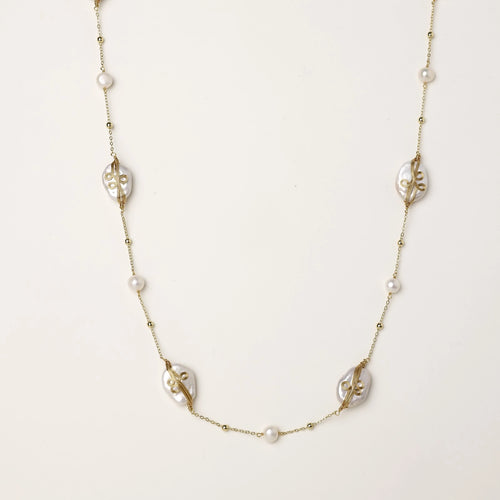 Delicate gold-plated necklace featuring translucent leaf-shaped baroque pearls and round freshwater pearls on neutral background.