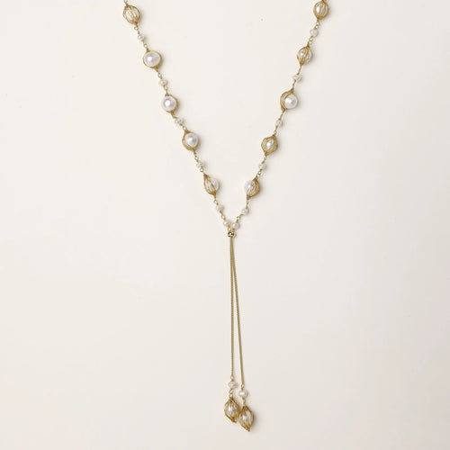 Long gold-plated lariat necklace with wire-wrapped freshwater pearls and chain tassel detail on cream background.