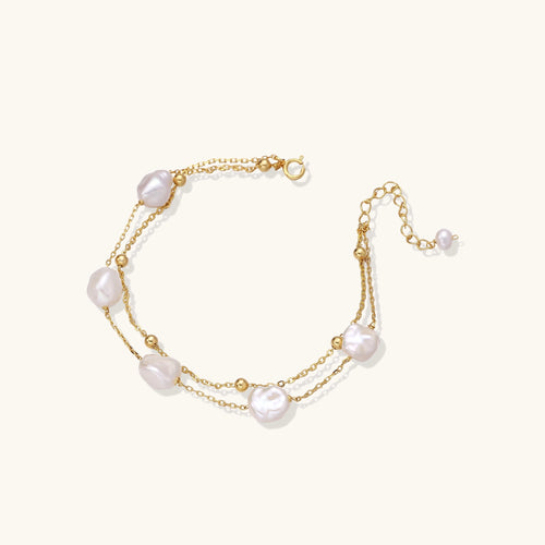 Delicate multi-layered gold-plated bracelet with irregular baroque pearls and freshwater pearls on cream background.