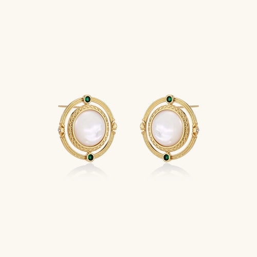 Close-up of gold-plated circular earrings with white mother-of-pearl centers and green zirconia accents on cream background.