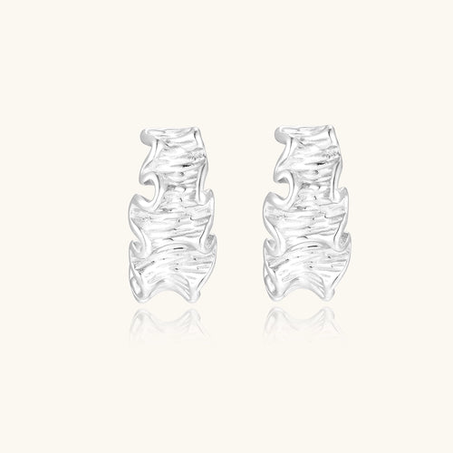 Textured gold-plated hoop earrings with flowing ripple design displayed on clean white background.