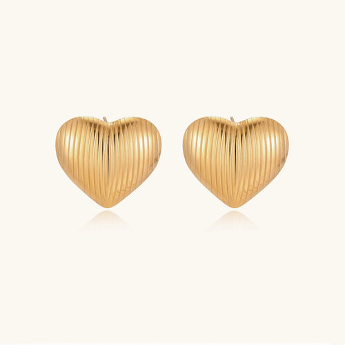 Close-up of ridged heart-shaped gold-plated stud earrings with textured surface pattern on cream background.